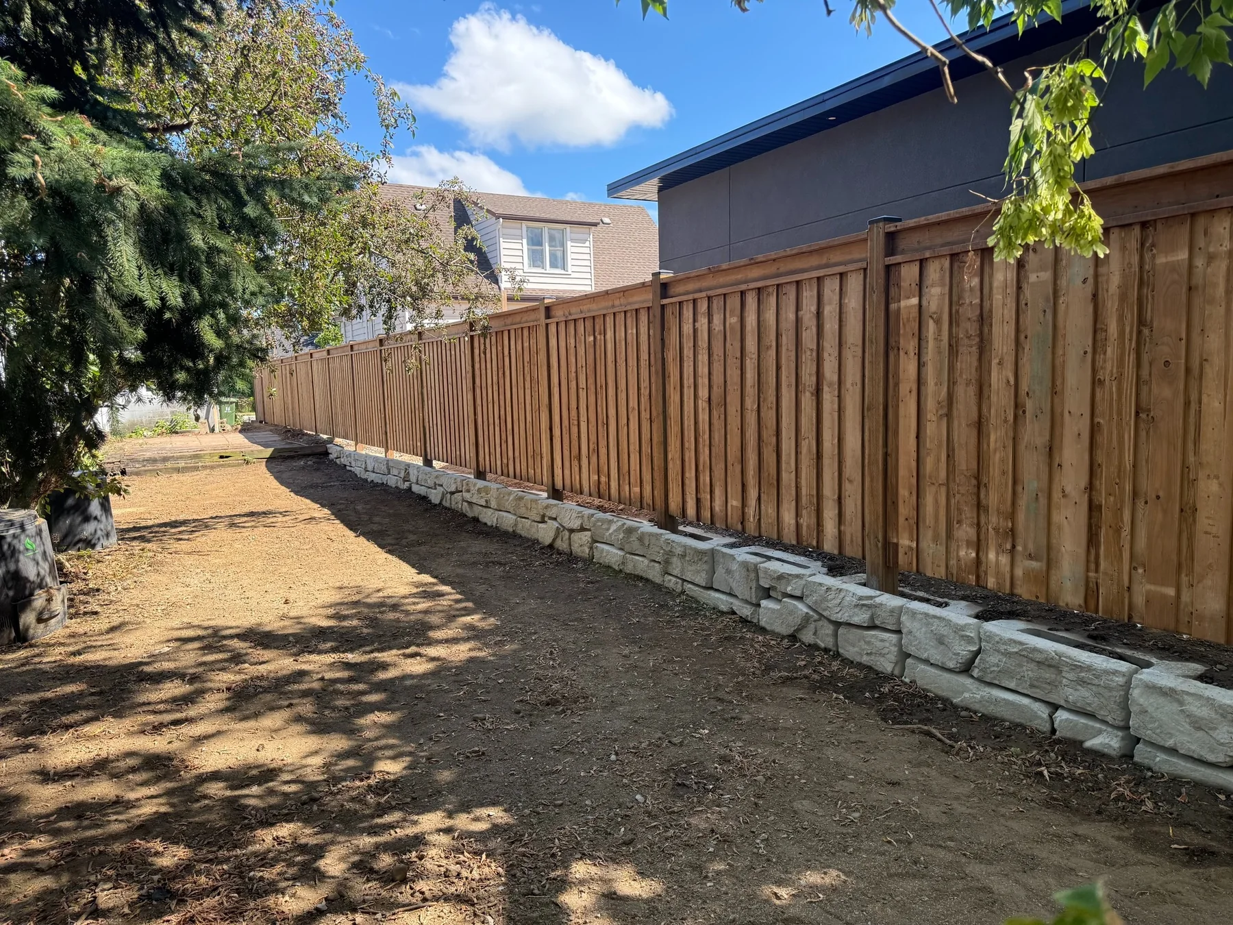 Completed wood privacy fence above a stone retaining wall by Garden City Group